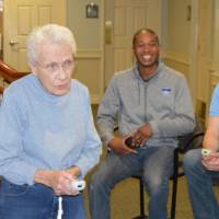 A senior plays a game of Wii Bowling while two volunteers watch.